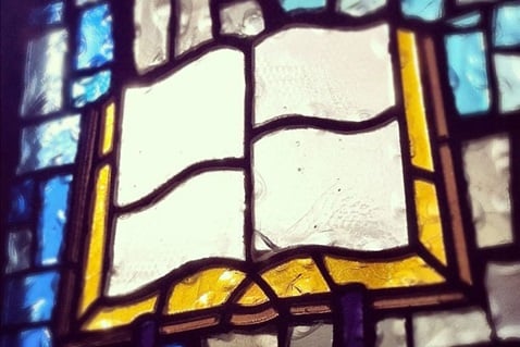 Photo of a stained glass window that shows the Bible.  We believe that the Bible is the primary authority for our faith and practice.