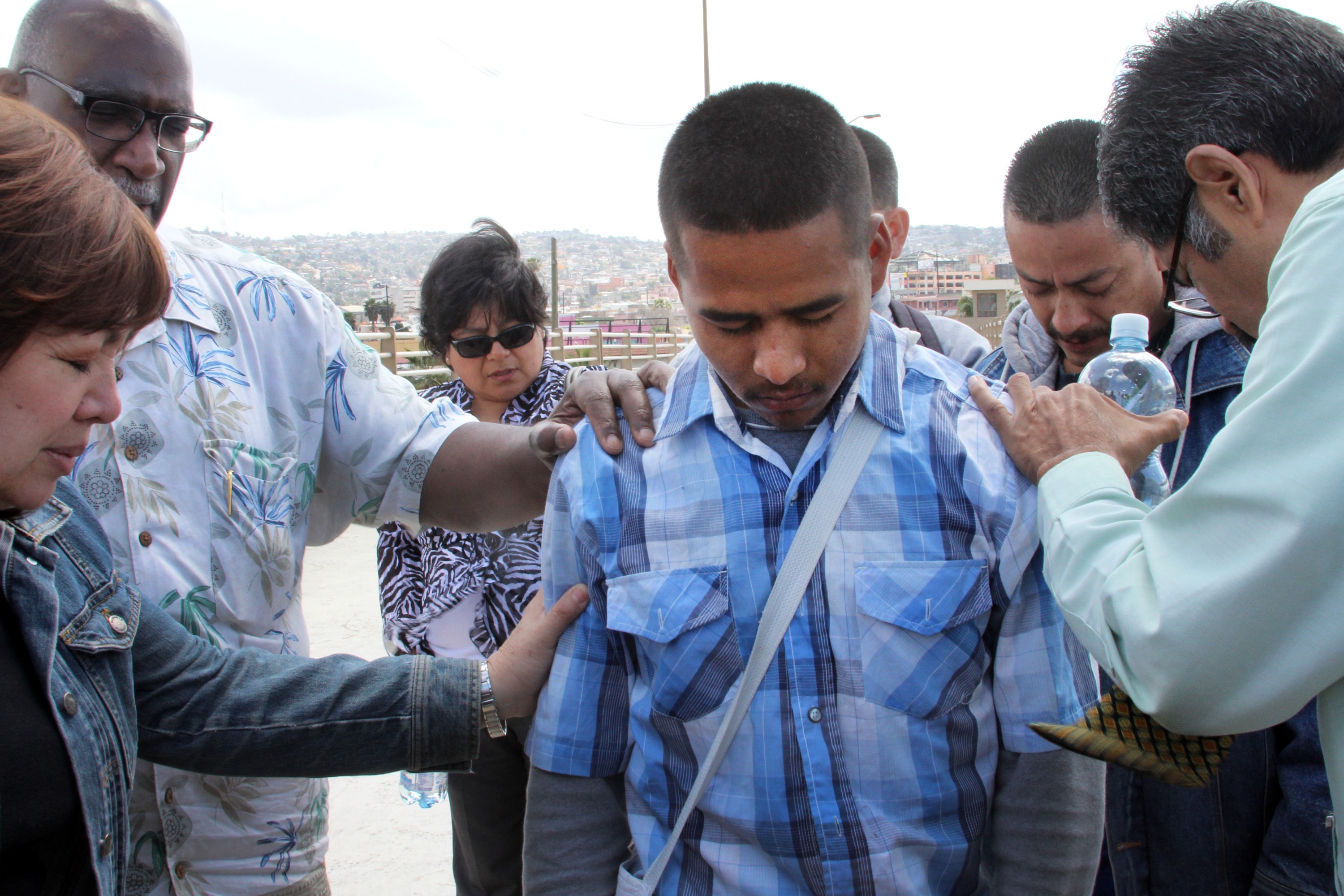 Bishop Minerva Carcaño, Bishop Gregory Palmer and others prayer with a young man, Angelo Mondragon, on the Mexico Bridge. Photo by Kathleen Barry, UMNS