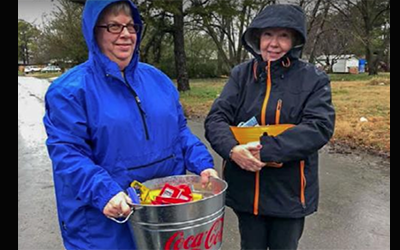 Two Volunteers help pass out snacks to kids during cold and wet weather.