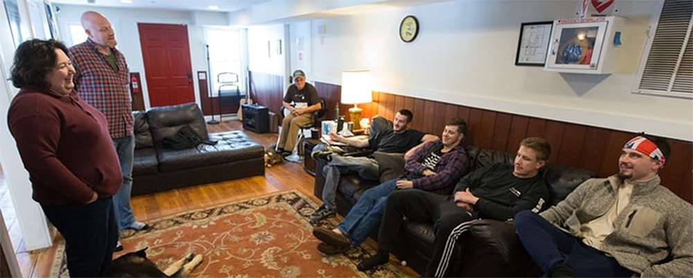 The Rev. Cheryl George (left) visits with Sloan (right) and other recovering addicts at Jacob’s Ladder. Standing with George is Chad Bishop, director of operations for the recovery home.