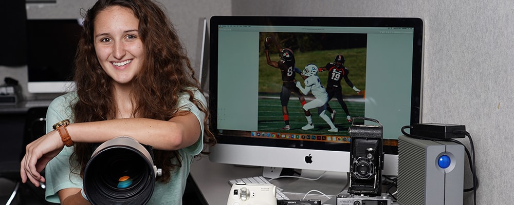Lyndy Lynch poses in front of her computer desk with her favorite tool, her camera. Courtesy photo.