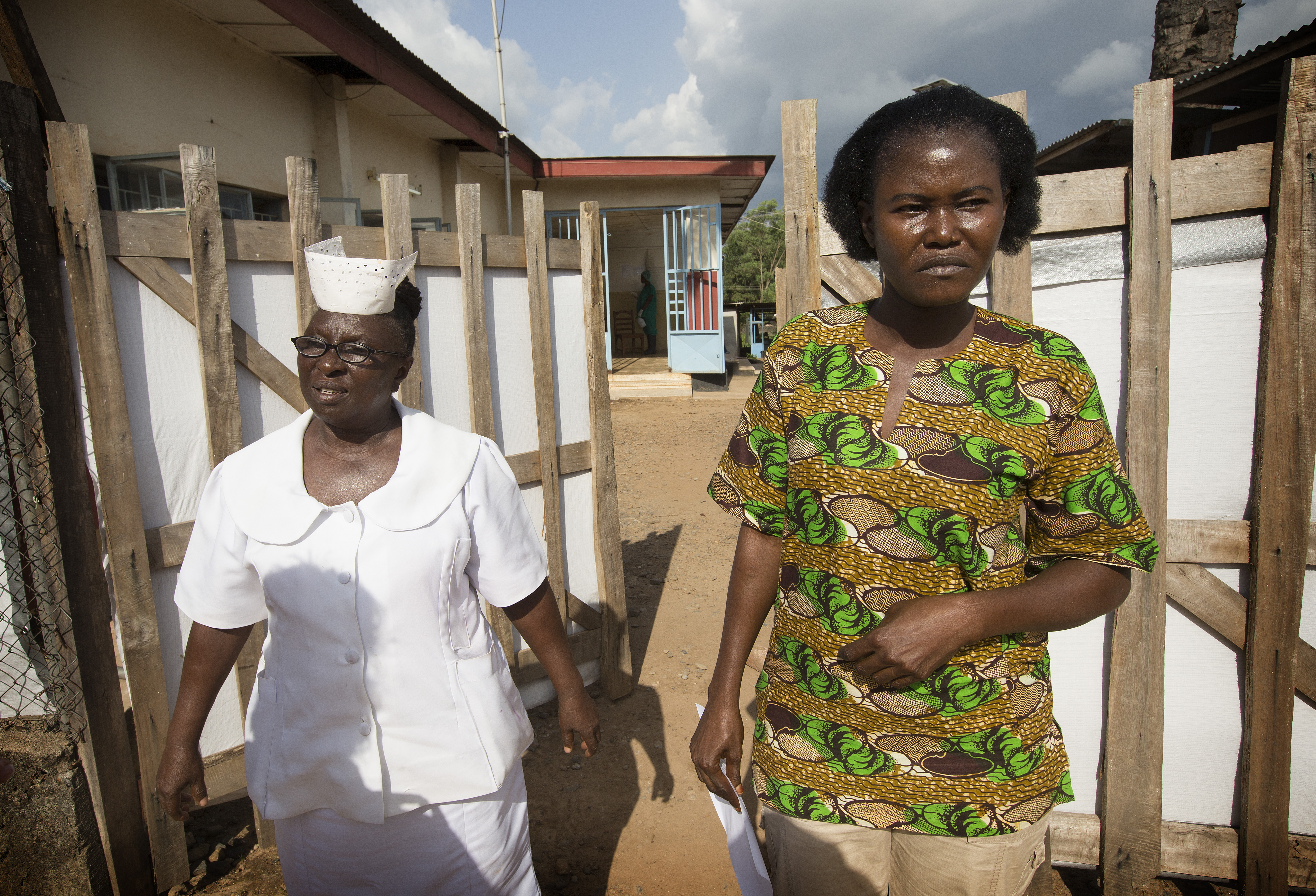 Mbalu Fonnie, head nurse in the hemorrhagic fever ward, and nurse Veronica Karoma describe efforts to contain the Ebola virus as they stand outside the gates to the isolation ward at the government hospital in Kenema, Sierra Leone. Photo by Mike DuBose, UM News.