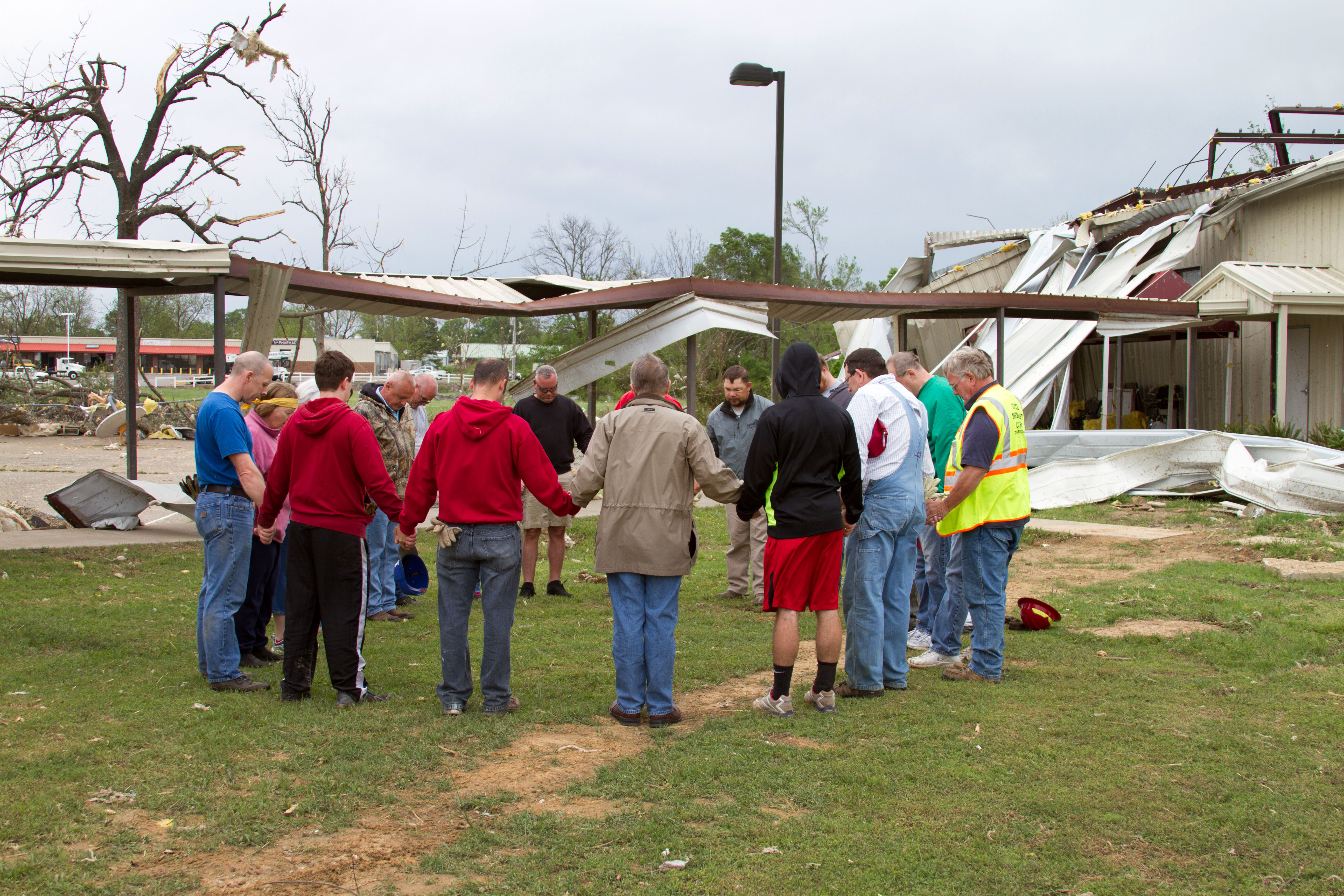 Bishop Gary Mueller (in brown jacket, back to the camera) prays for and with members of Vilonia UMC who are helping with clean-up on April 29, 2014, in the wake of the tornado that ripped through the central Arkansas town two days earlier. Photo by Amy Forbus, Arkansas United Methodist.