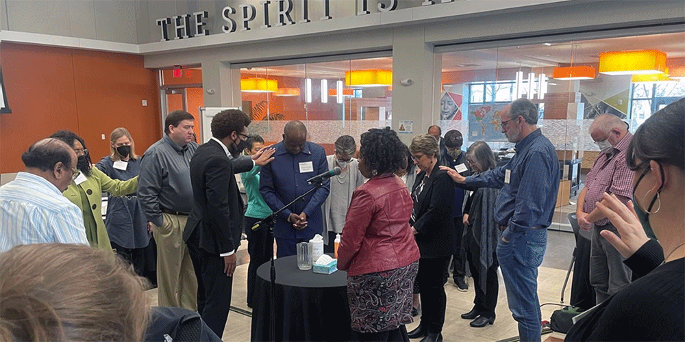 Members of the Connectional Table lay hands on Bishop Mande Muyombo (center), chair of the Connectional Table, and Judi Kenaston (fourth from right), interim chief connectional ministries officer, during the group’s meeting Feb. 24 in Atlanta. The leadership body helps determine the budget of The United Methodist Church. Photo by Jim Patterson, UM News.