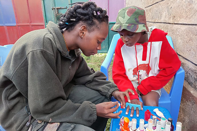 Gloria Kache (à gauche) fait la manucure à Clementina Kalunde à l’Église Méthodiste Unie Parkview Kitengela, à Nairobi, au Kenya. Gloria Kache bénéficie du programme « No Girl No Cry » mis en place par l’église, qui vise à autonomiser les jeunes filles de la communauté grâce à l’éducation et au mentorat. Elle est aujourd’hui bénévole au centre éducatif Mumo de l’église. Photo de Jackline Mwende.