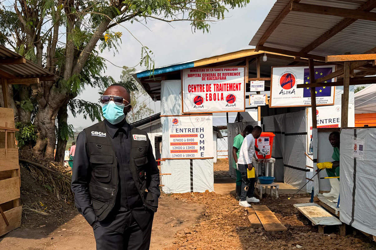 Le Dr Damas Lushima, portant un masque et un gilet de Global Ministries, se tient devant le centre de traitement d’Ebola de l’hôpital général de référence de Rwampara, à Bunia. En tant que coordinateur du département de la santé de la région épiscopale du Congo Est, il supervise la réponse intégrée de l’Église Méthodiste Unie face à la 17e épidémie d’Ebola qui touche la province d’Ituri. Photo gracieusement fournie par le Conseil de santé du Congo Est.