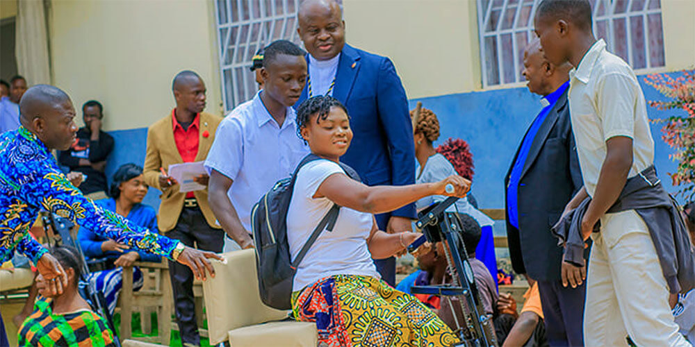 A young girl with limited mobility smiles as she maneuvers her tricycle equipped with hand cranks for the first time as Bishop Mande Muyombo (standing at center) and other church leaders look on. This project aims to promote social and educational inclusion by enabling young people and adults to travel with dignity to their places of work or study. Photo by Yamba Kisonga Barthélémy, UM News.