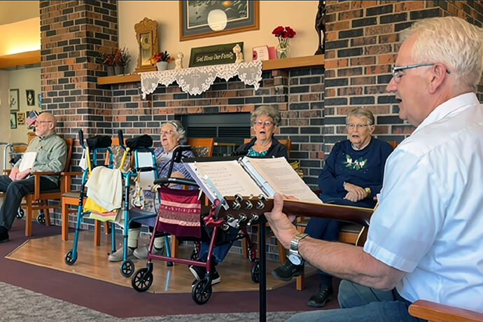 Pastor Dean Roush (right) and volunteers from Mora United Methodist Church in Minnesota sing with residents of a nursing home as part of the church’s community outreach. A free bread giveaway and weekly coffee chat also provide opportunities for church members to be in fellowship with their community. Video image by Lilla Marigza, UM News. 