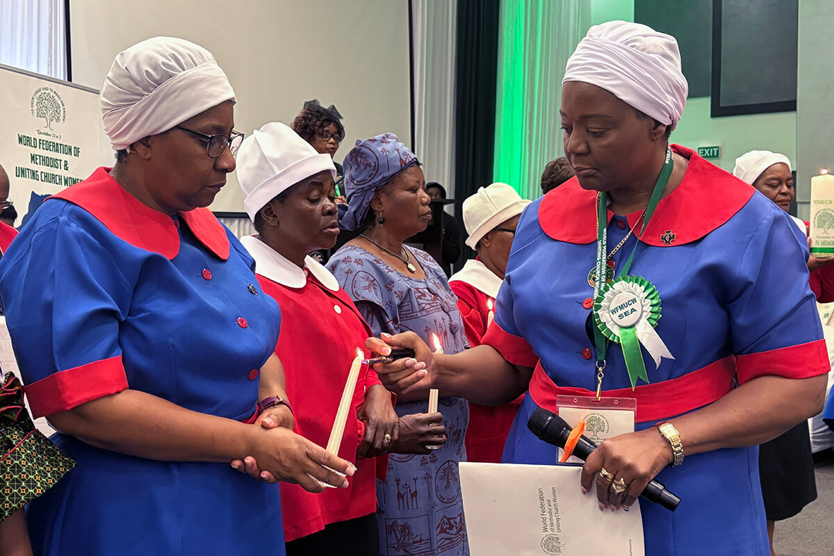 Patricia Petudzai Mapani allume une bougie tenue par Tabitha Mushishi, coordinatrice de l'Église Méthodiste Unie au Zimbabwe, lors d'un service commémoratif en hommage aux membres de la Fédération Mondiale des Femmes des Églises Méthodistes et Unifiées au Botswana, en avril 2025. Photo : Eveline Chikwanah, UM News.