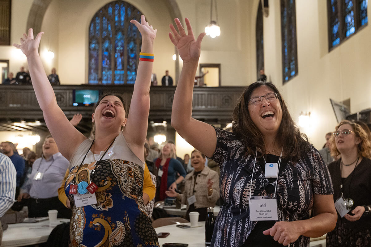 Ashlee Vitz (à gauche) et Teri Watanabe lèvent les bras en signe de louange lors du culte d’ouverture, le 21 octobre, à l’occasion du Rassemblement des responsables de l’Église Méthodiste Unie à la Knox United Church de Calgary, au Canada. Cet événement, qui se poursuit jusqu’au 24 octobre, rassemble des laïcs et des membres du clergé du monde entier afin d’imaginer un nouvel avenir pour l’Église Méthodiste Unie. Photo de Mike DuBose, UM News.